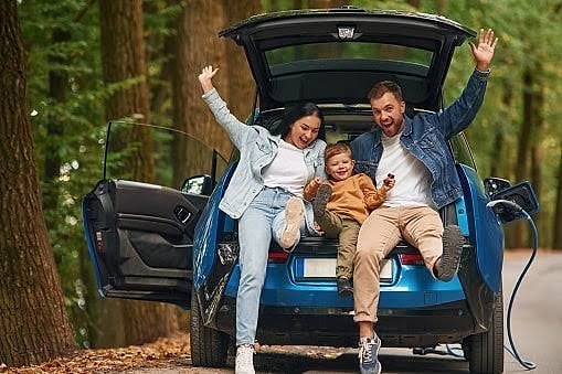 Family sitting in the open trunk of their electric car in the forest